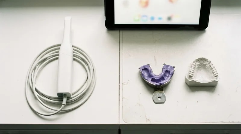 Intraoral scanner wand on one side and a putty impression tray with plaster cast on the other