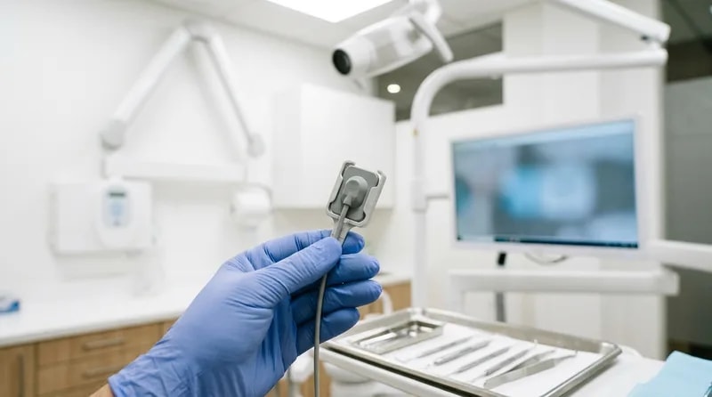 Digital dental x-ray sensor on a clinical tray beside a modern imaging arm in a treatment room